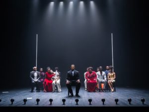 Actors are sitting on the stage looking Forward